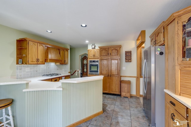 kitchen with decorative backsplash, stainless steel appliances, custom range hood, light countertops, and a peninsula