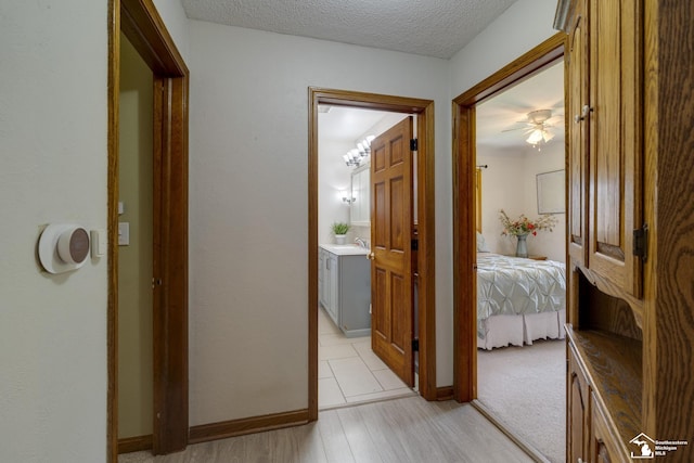 corridor with a textured ceiling, a sink, light wood-style flooring, and baseboards