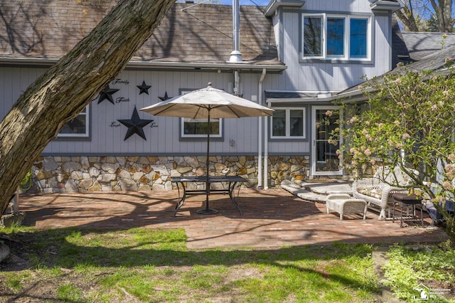 rear view of property featuring a patio area, a shingled roof, and stone siding