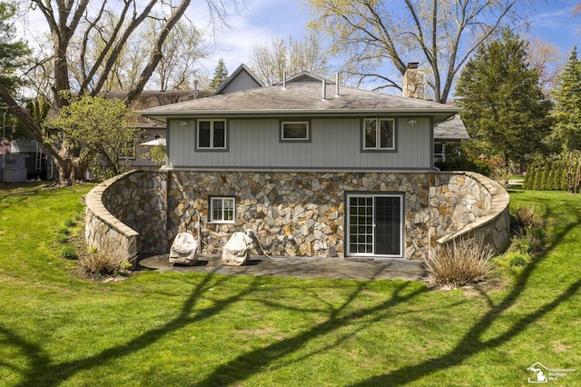 back of property with a lawn, stone siding, a patio area, and a chimney