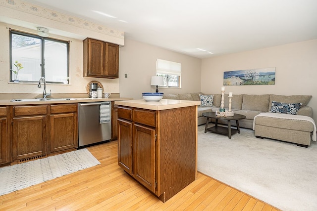 kitchen with a healthy amount of sunlight, dishwasher, a sink, open floor plan, and light wood-style floors