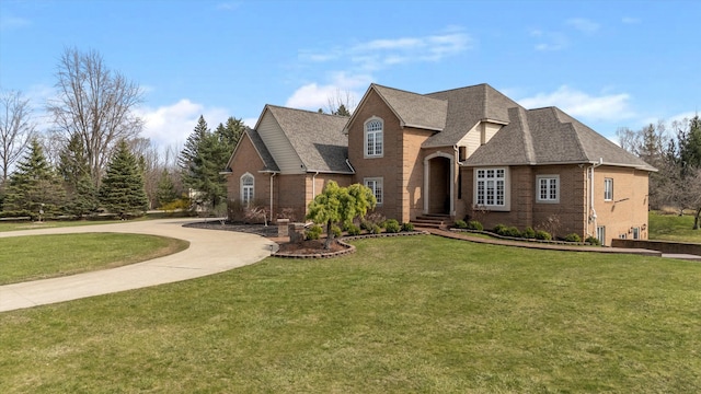 view of front of house with a front yard, a shingled roof, curved driveway, and brick siding