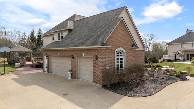 view of side of home with brick siding, a gazebo, a shingled roof, and concrete driveway