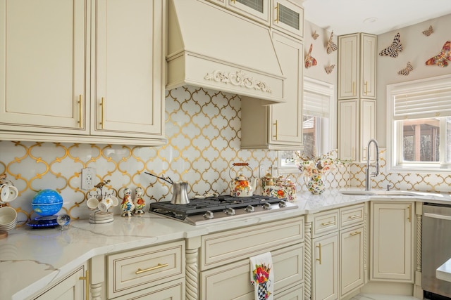 kitchen featuring a sink, appliances with stainless steel finishes, light stone countertops, cream cabinets, and custom exhaust hood