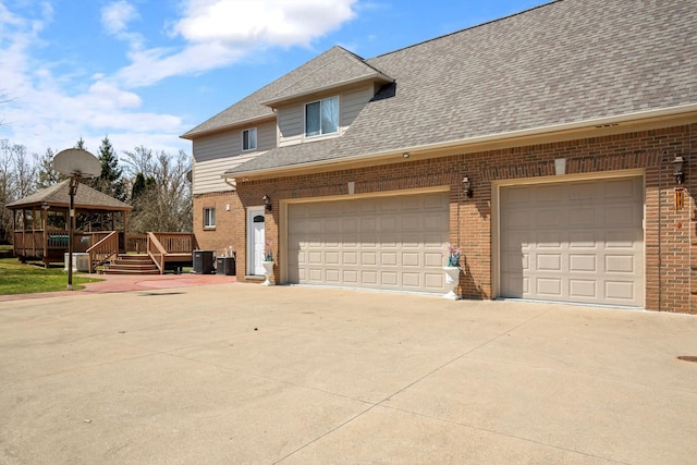 exterior space featuring a gazebo, concrete driveway, a shingled roof, and brick siding