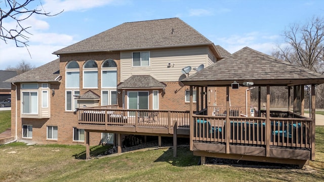 rear view of house featuring a deck, brick siding, a gazebo, and roof with shingles