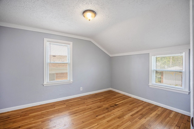 bonus room featuring light wood finished floors, a textured ceiling, vaulted ceiling, and a healthy amount of sunlight