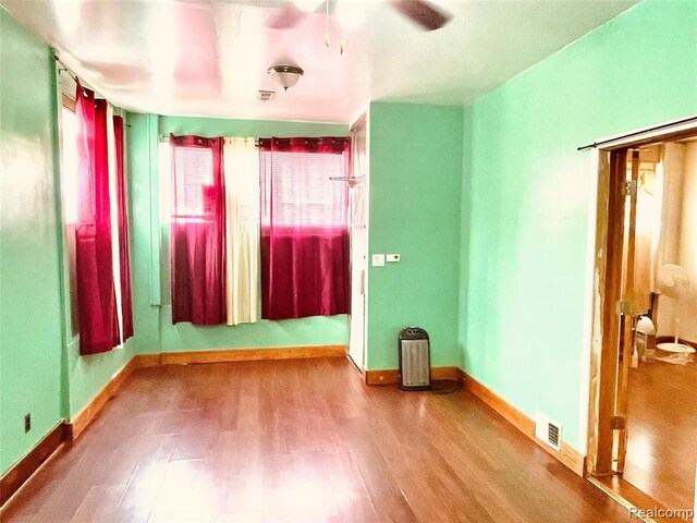 empty room with wood finished floors, a ceiling fan, and baseboards
