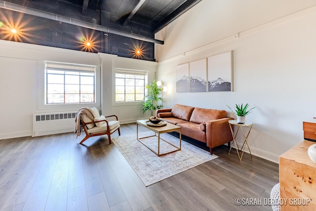 living area with radiator, a towering ceiling, wood finished floors, and baseboards