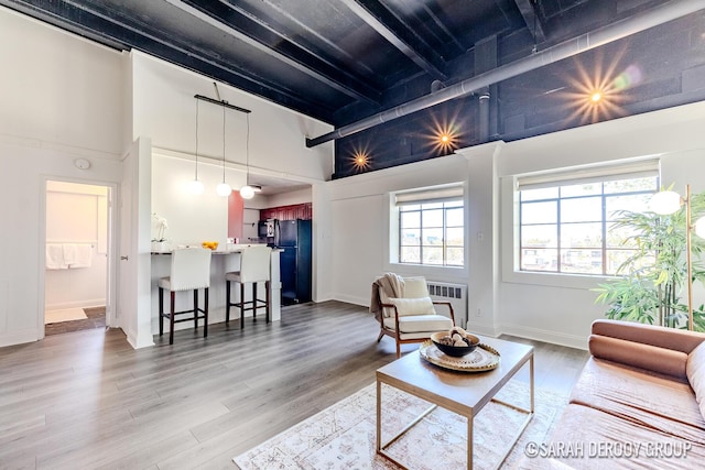 living area featuring beam ceiling, a towering ceiling, and light wood-style flooring