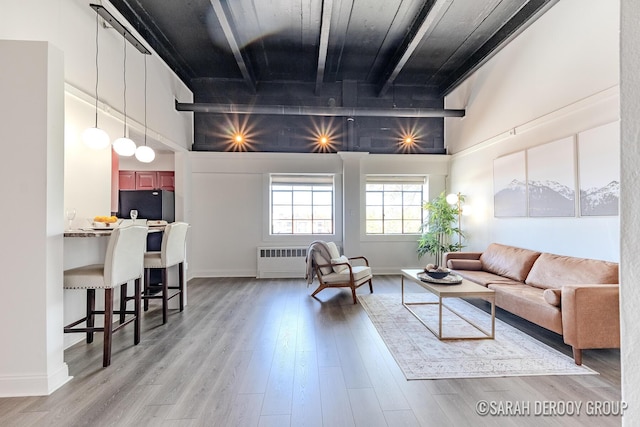 living area featuring radiator heating unit, a towering ceiling, light wood finished floors, and baseboards