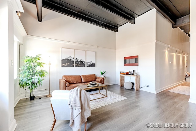 living area with beam ceiling, baseboards, light wood-style floors, and a high ceiling