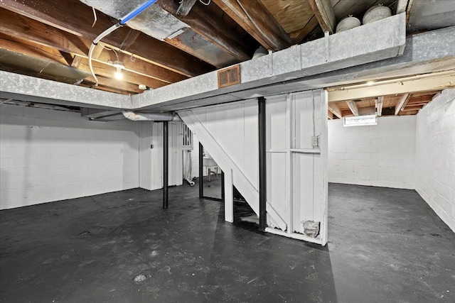 unfinished basement featuring stairs, concrete block wall, and visible vents