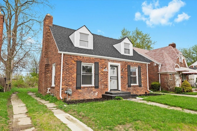 cape cod-style house featuring roof with shingles, a chimney, a front yard, and brick siding