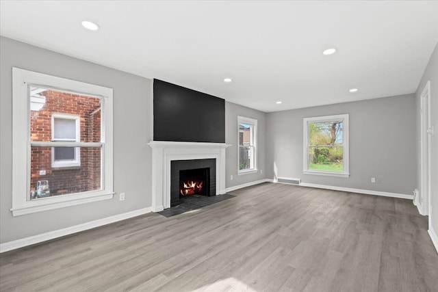 unfurnished living room featuring a fireplace with flush hearth, baseboards, wood finished floors, and visible vents