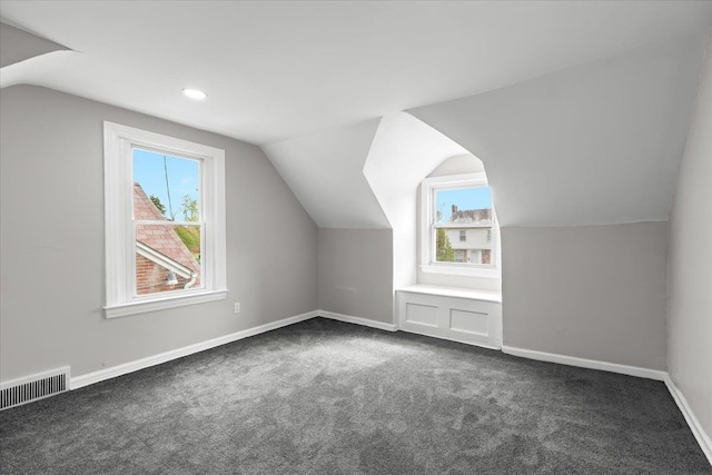 bonus room with visible vents, lofted ceiling, a wealth of natural light, and dark colored carpet