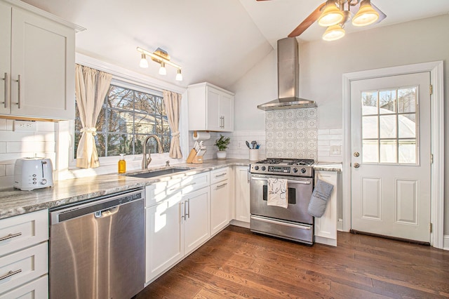 kitchen with a ceiling fan, a sink, lofted ceiling, stainless steel appliances, and wall chimney exhaust hood