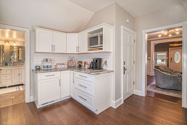 kitchen with backsplash, stainless steel microwave, dark wood finished floors, and light stone countertops