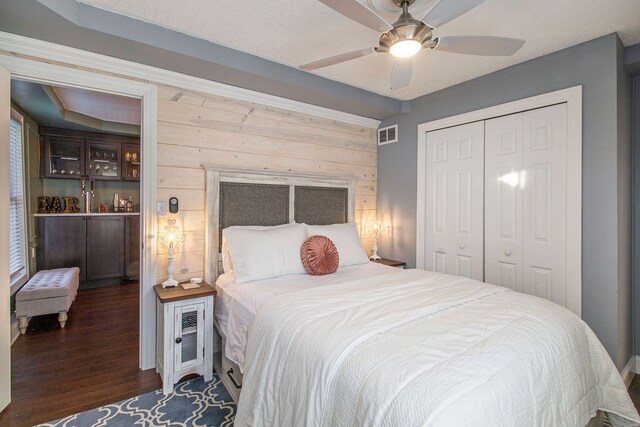 bedroom with a ceiling fan, visible vents, wood walls, wood finished floors, and a closet