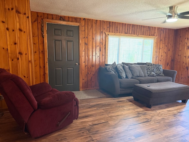 living room with a textured ceiling, ceiling fan, wood walls, and wood finished floors