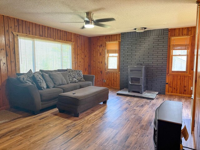 living room with a wood stove, a ceiling fan, wood walls, a textured ceiling, and wood finished floors