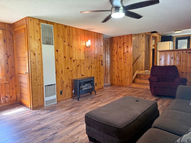 living area with a wood stove, a heating unit, a ceiling fan, wood walls, and wood finished floors