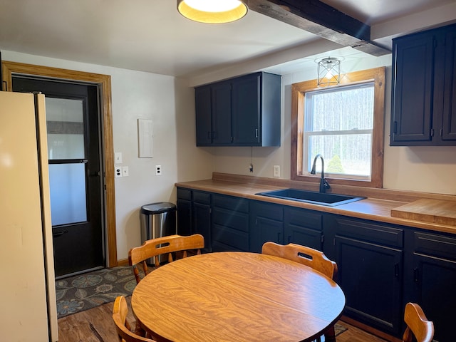 kitchen with a sink, light countertops, blue cabinets, freestanding refrigerator, and dark wood-style flooring
