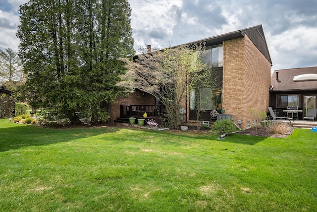 back of house featuring a lawn, a deck, and brick siding