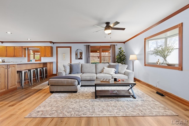 living area with light wood-type flooring, crown molding, a ceiling fan, visible vents, and baseboards