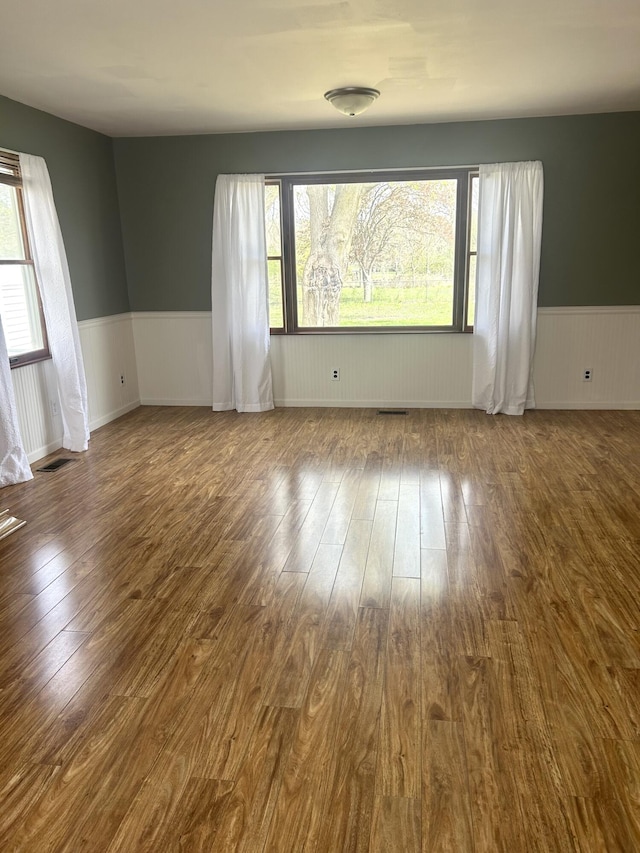 spare room with a wainscoted wall, a wealth of natural light, and dark wood-type flooring