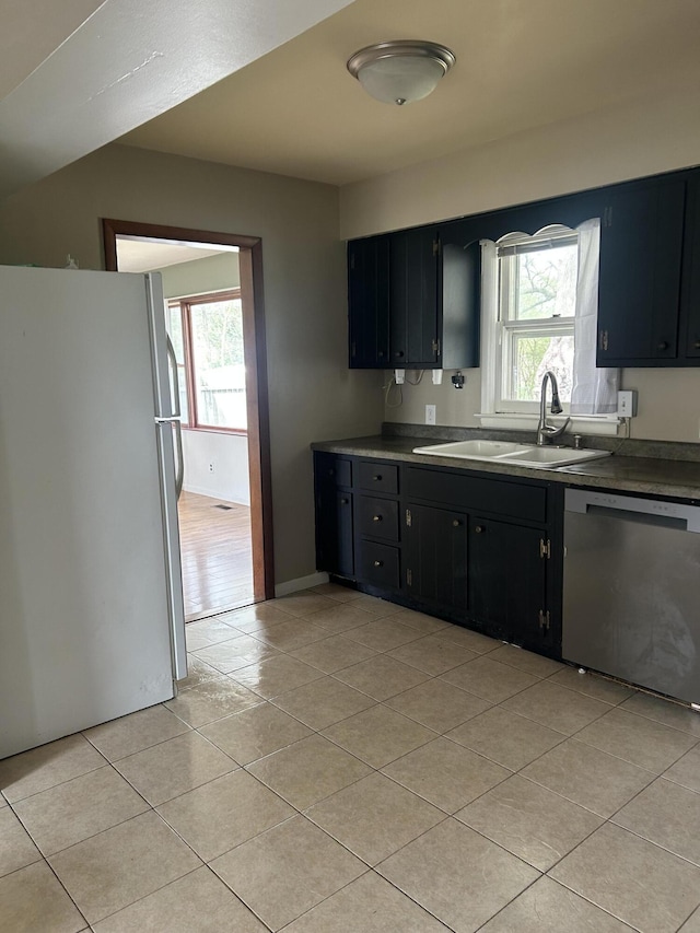 kitchen featuring stainless steel dishwasher, dark cabinets, freestanding refrigerator, light tile patterned floors, and a sink