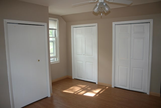 unfurnished bedroom featuring wood finished floors, multiple closets, vaulted ceiling, and baseboards