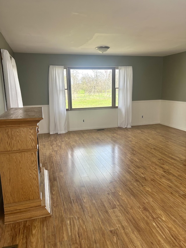 empty room featuring wood finished floors, visible vents, and wainscoting