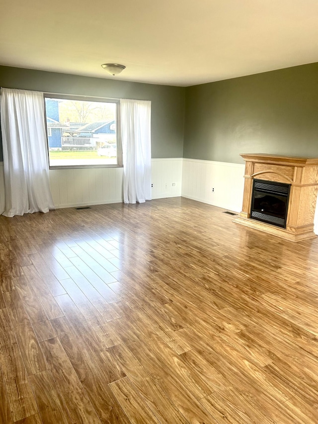 unfurnished living room featuring wainscoting, wood finished floors, and a glass covered fireplace