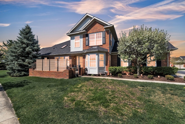 view of front of property featuring brick siding, a front yard, and roof with shingles