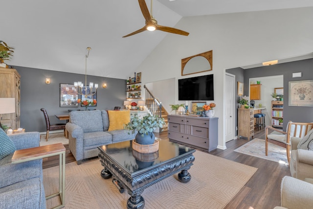 living room featuring high vaulted ceiling, ceiling fan with notable chandelier, stairs, baseboards, and wood finished floors
