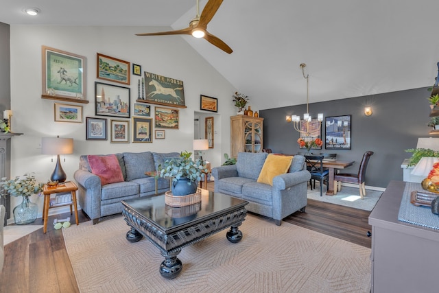 living room featuring baseboards, high vaulted ceiling, wood finished floors, and ceiling fan with notable chandelier