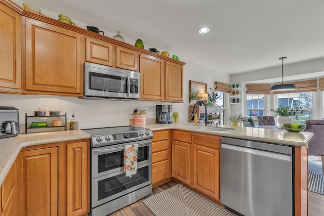 kitchen with appliances with stainless steel finishes, a sink, light countertops, light wood-style flooring, and a peninsula
