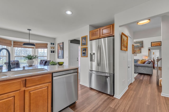 kitchen featuring appliances with stainless steel finishes, brown cabinets, a sink, baseboards, and dark wood-type flooring