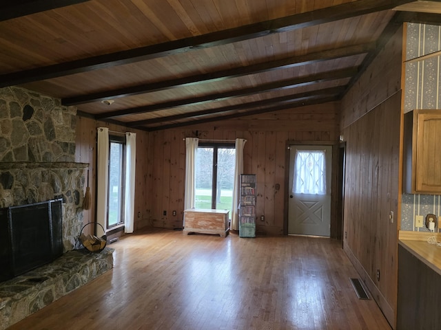 unfurnished living room featuring wood finished floors, a healthy amount of sunlight, lofted ceiling with beams, and a stone fireplace