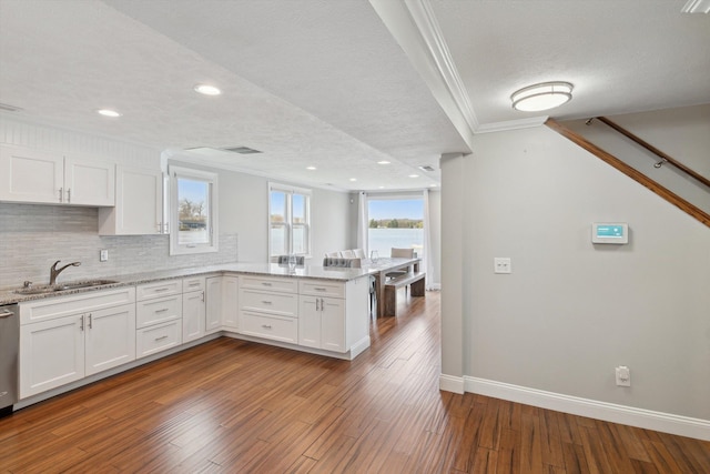 kitchen with crown molding, a peninsula, baseboards, white cabinets, and a sink