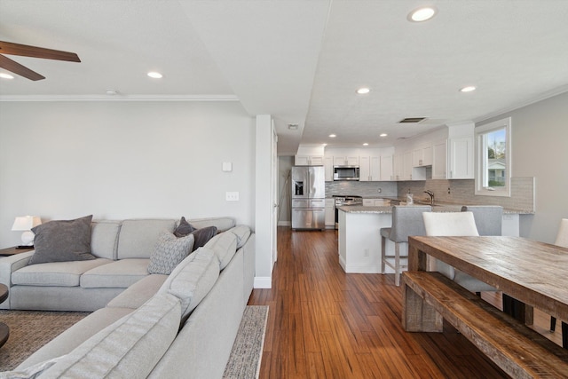 living room with crown molding, baseboards, ceiling fan, recessed lighting, and dark wood finished floors