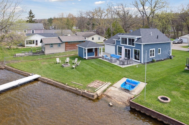 back of house with a water view, an outdoor living space with a fire pit, roof with shingles, and a yard