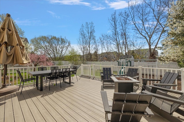 wooden terrace featuring an outdoor fire pit, an outdoor structure, a fenced backyard, a storage shed, and outdoor dining space