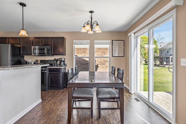 kitchen with dark wood finished floors, appliances with stainless steel finishes, dark brown cabinets, pendant lighting, and a notable chandelier