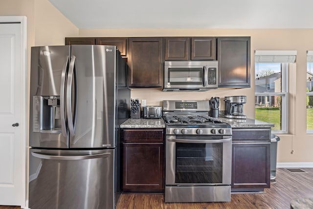 kitchen with light stone countertops, dark brown cabinetry, baseboards, appliances with stainless steel finishes, and dark wood finished floors