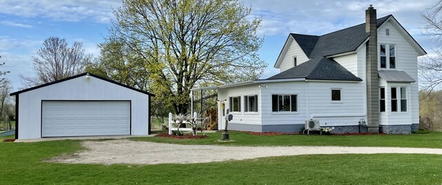 view of side of property featuring roof with shingles, a detached garage, a chimney, a lawn, and an outdoor structure