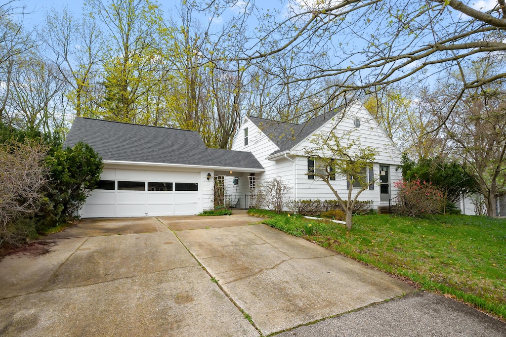 view of front of home with a front lawn, driveway, an attached garage, and roof with shingles
