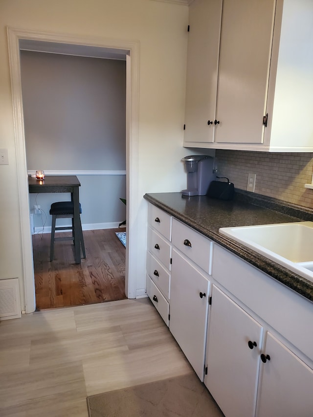 kitchen featuring dark countertops, white cabinets, backsplash, and visible vents