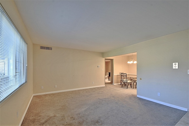 carpeted spare room with baseboards, a notable chandelier, and visible vents